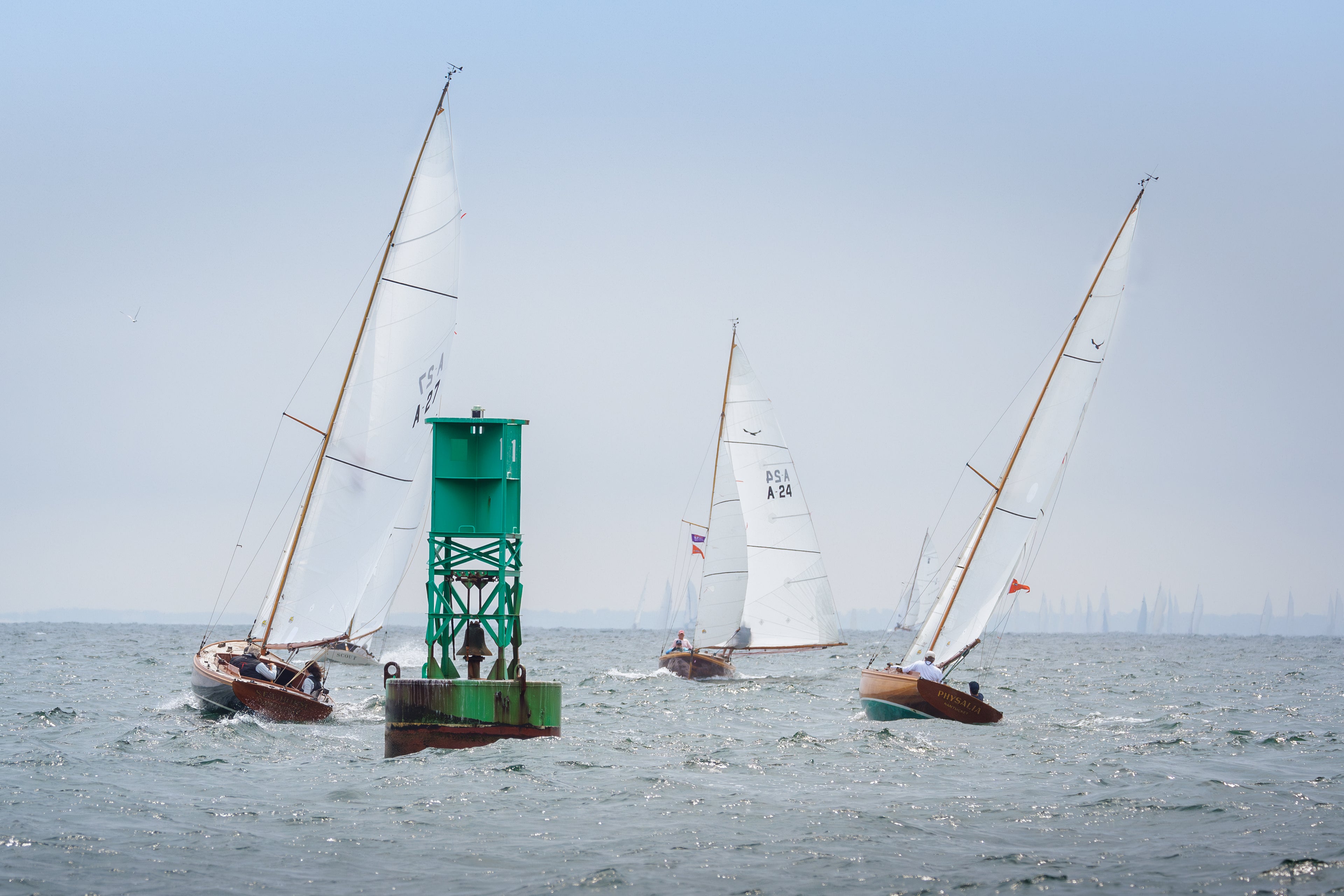Three sailboats near a green navigation buoy on a body of water.