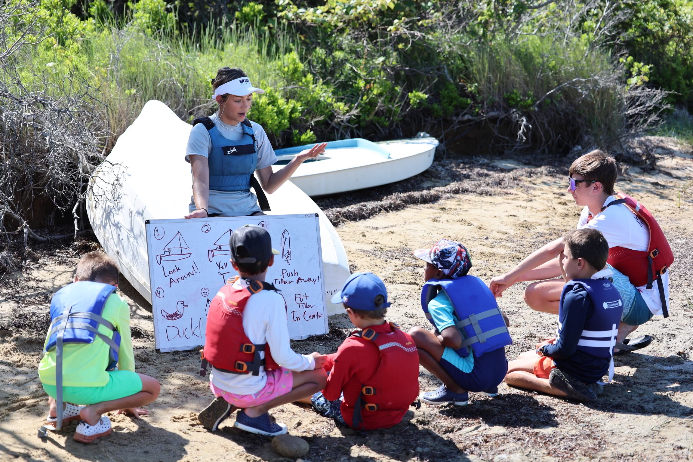 Educator with students outdoors near sailboats, teaching about water safety.