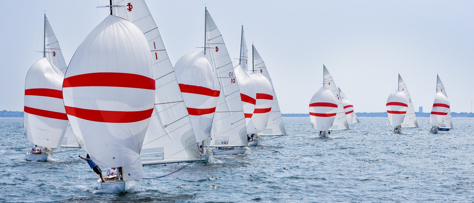 Multiple IODs with white sails and red stripes on a body of water.