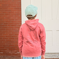 Person wearing a pink hoodie and blue shorts standing on steps with a brick wall and white door in the background.