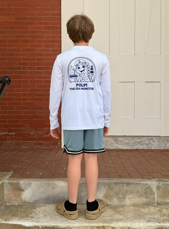 Child wearing a white long-sleeve shirt with a graphic design and text, standing outdoors.